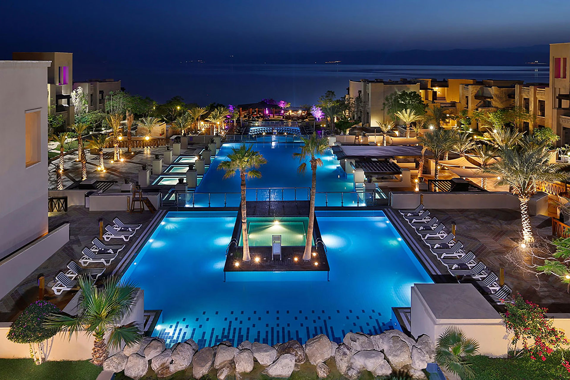 Luxury Dead Sea resort at night with illuminated pools and palm trees.