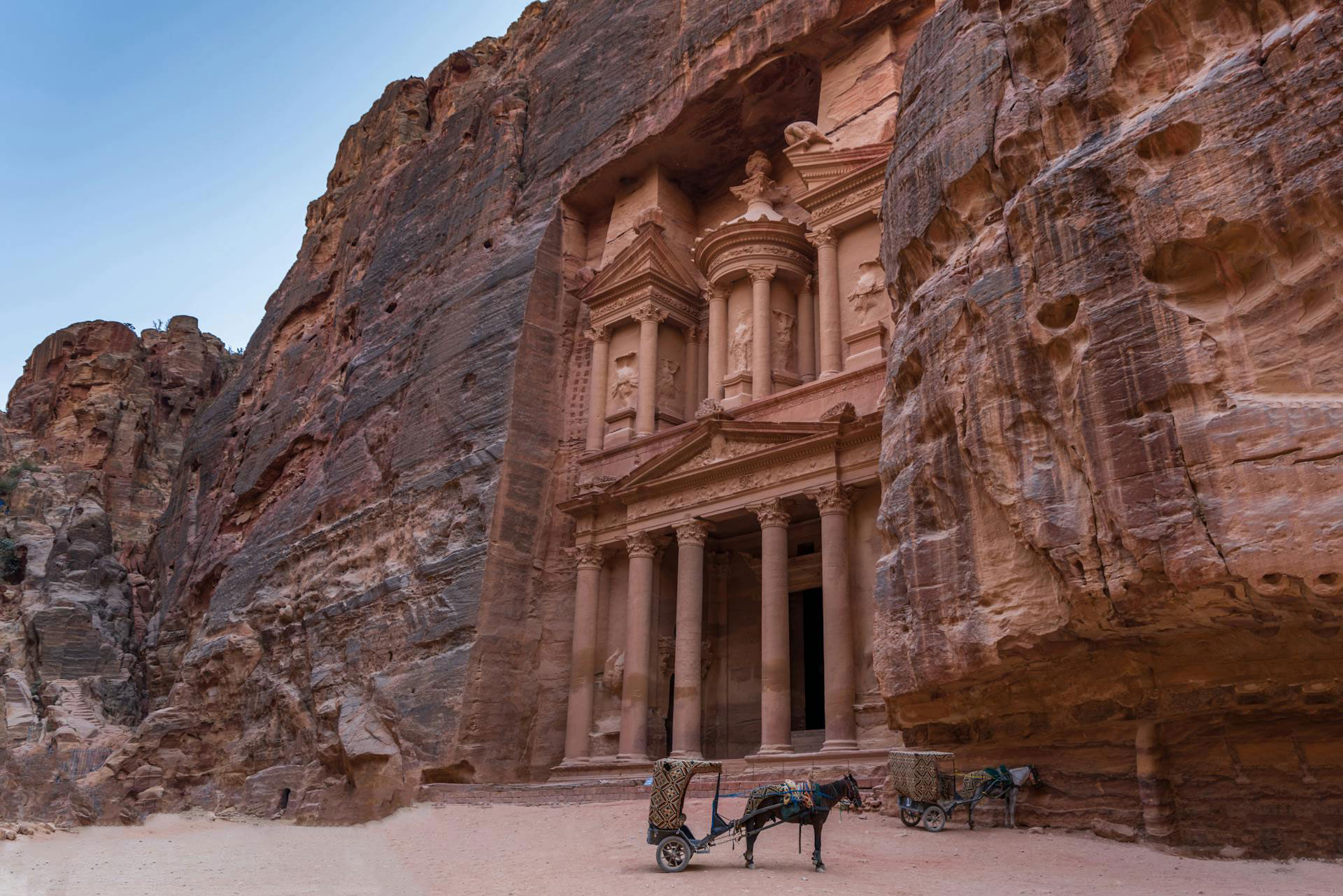 The Treasury (Al-Khazneh) in Petra, Jordan, carved into rose-red cliffs with horse carriages in front.