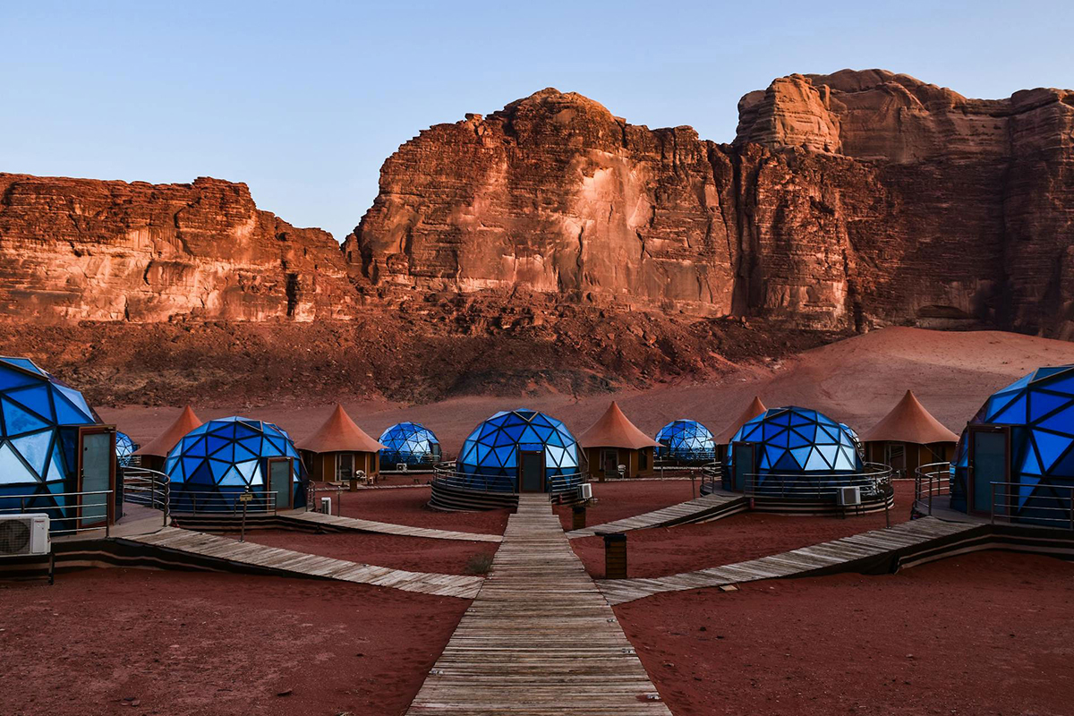 Luxury blue bubble dome tents in Wadi Rum desert, Jordan, with red sandstone mountains in the background.