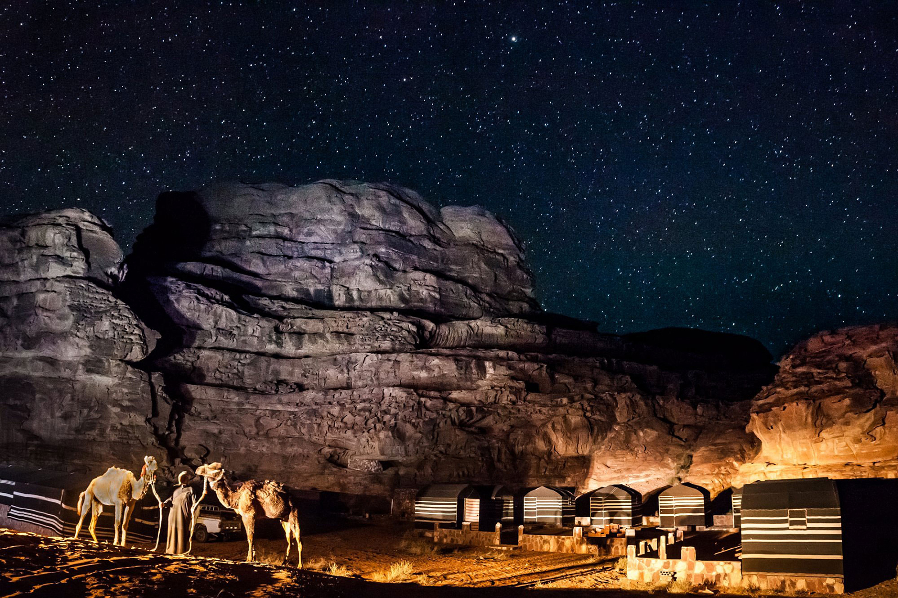 Bedouin camp in Wadi Rum desert at night with camels under a starry sky, Jordan.